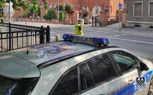 Na zdjęciu radiowóz oraz policjant przy przejściu dla pieszych.