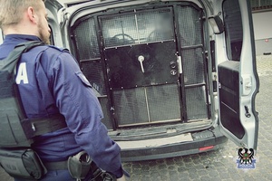 Na zdjęciu policjant zamyka drzwi radiowozu.